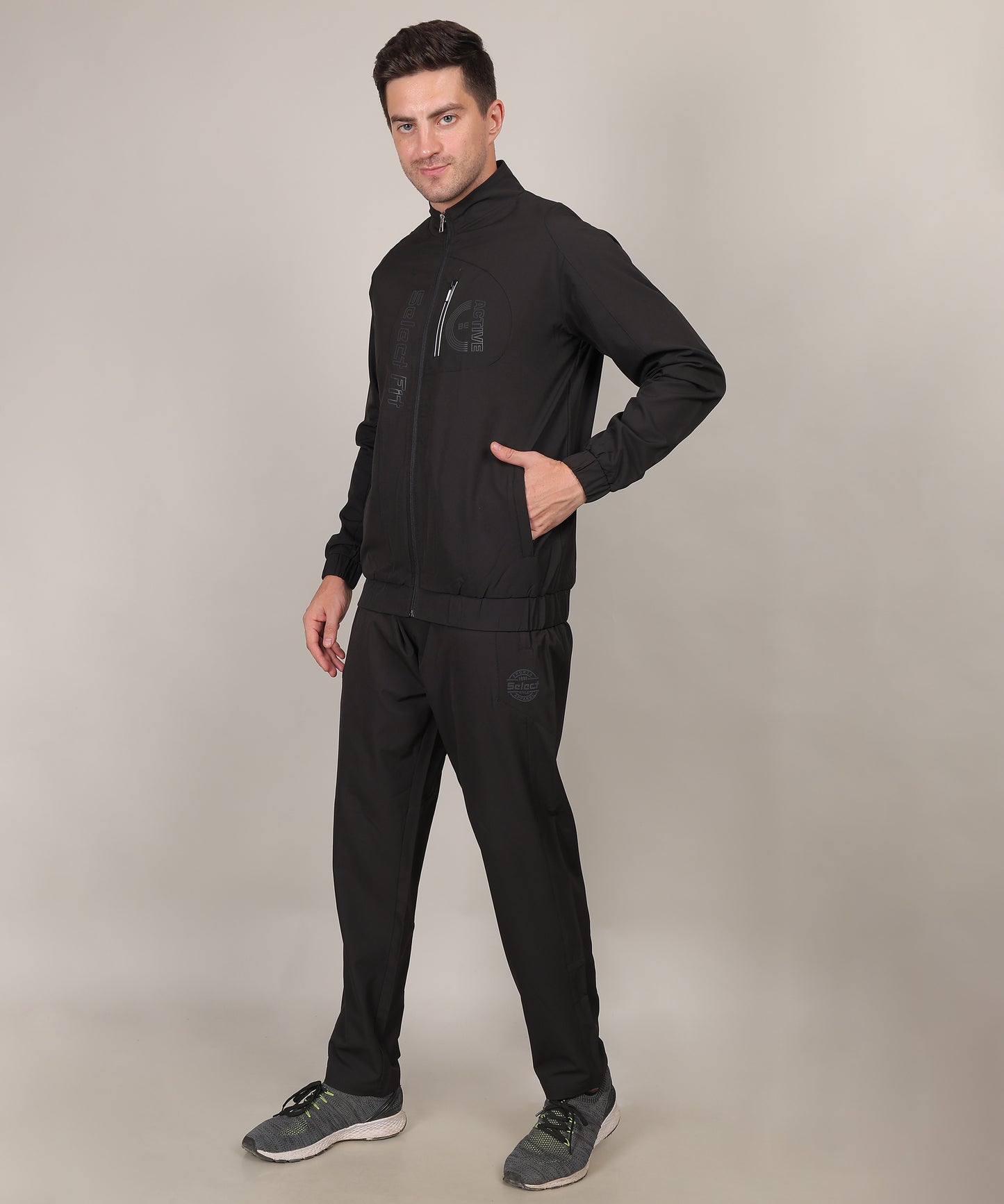 A man standing wearing a black tracksuit, consisting of black pants and a black jacket.