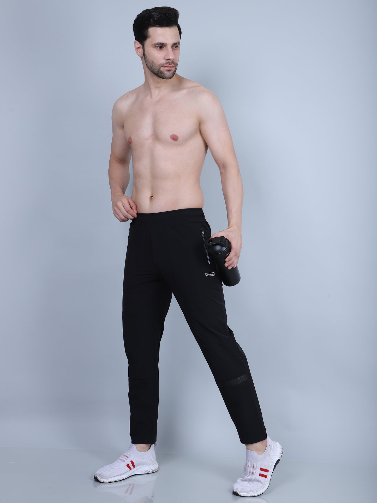 Man wearing black leggings holding a water bottle on a gray background