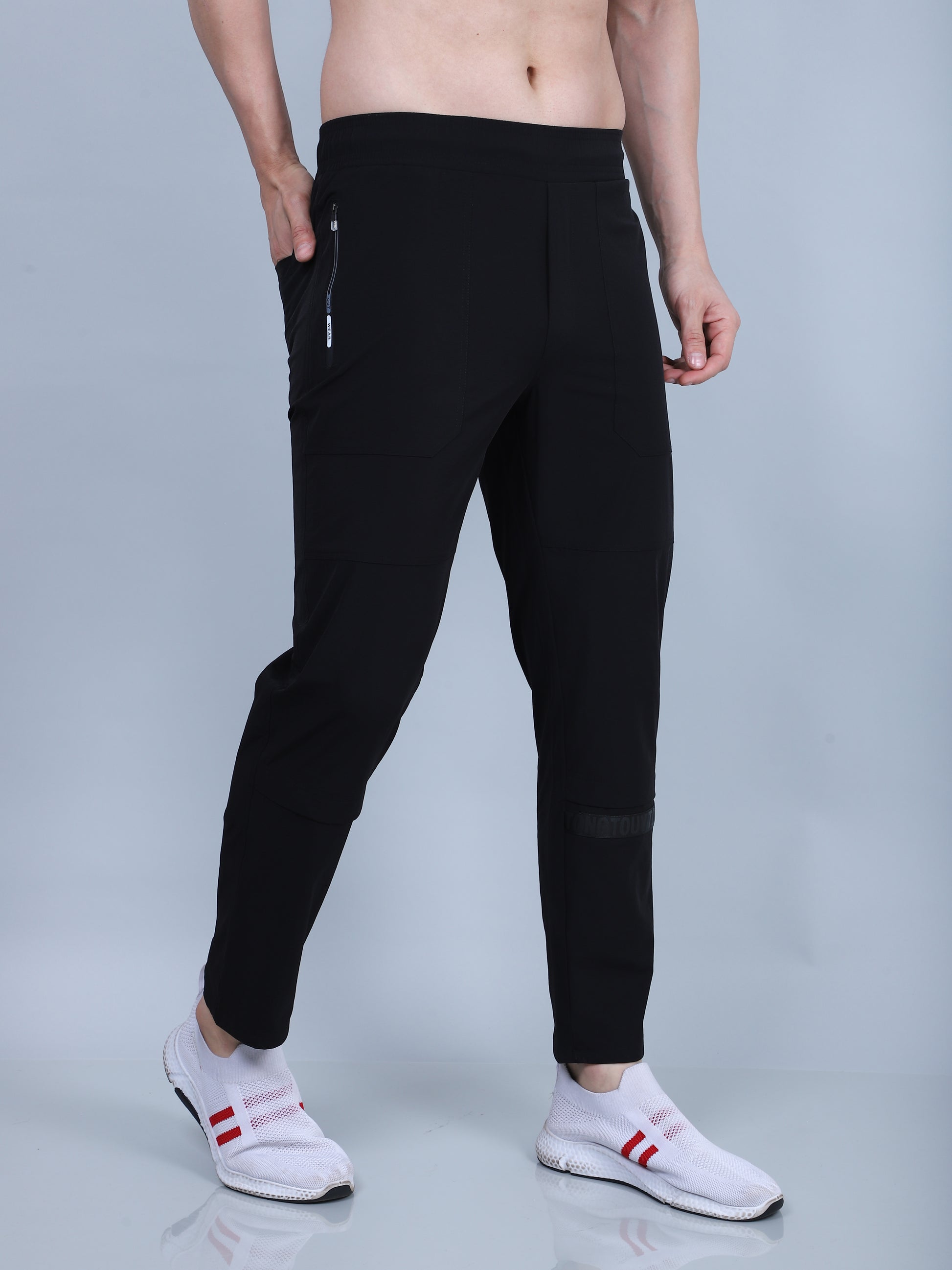 Person wearing black jogger pants with white sneakers on a gray background