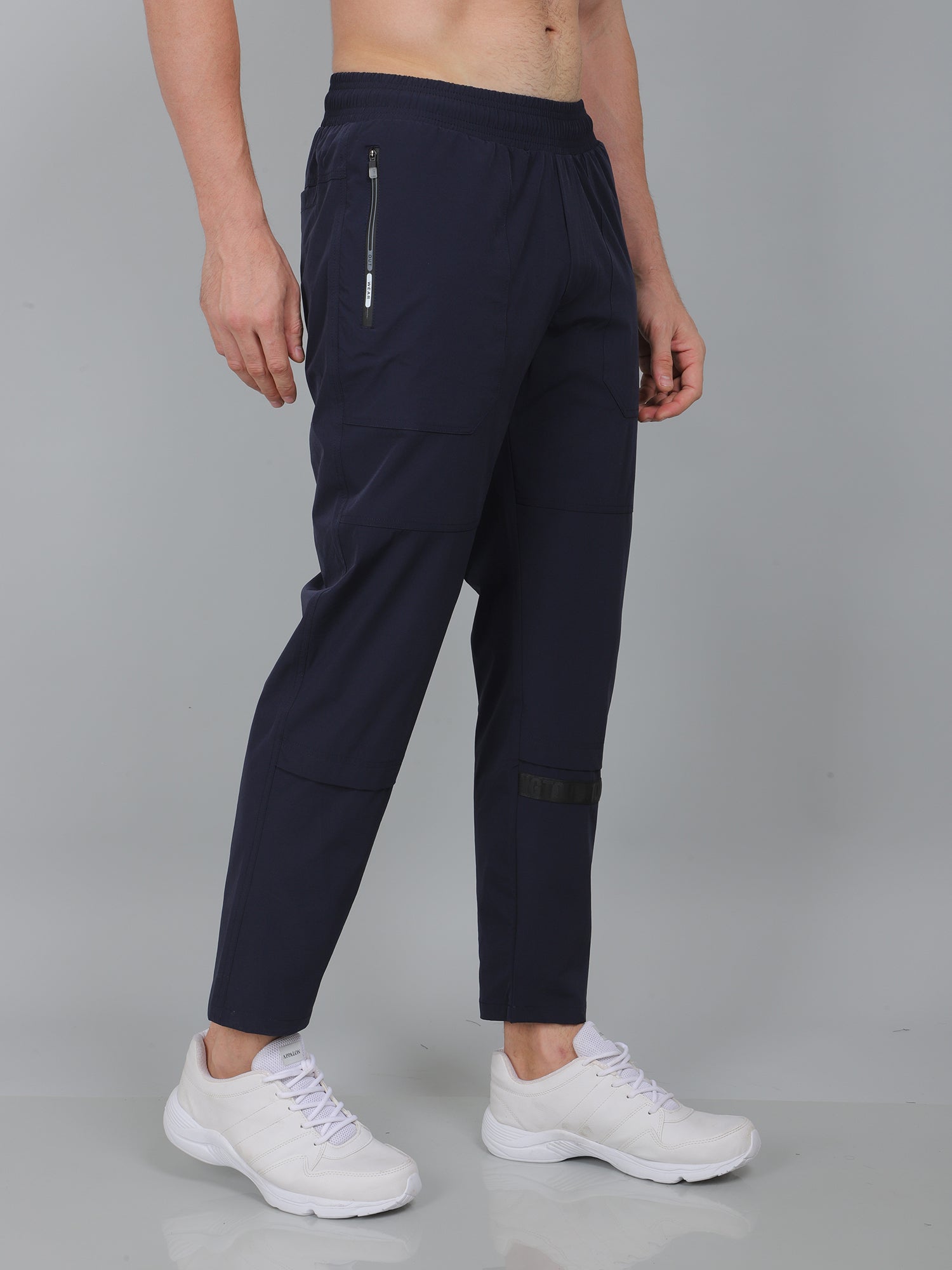 Person wearing navy blue pants with white sneakers on a gray background