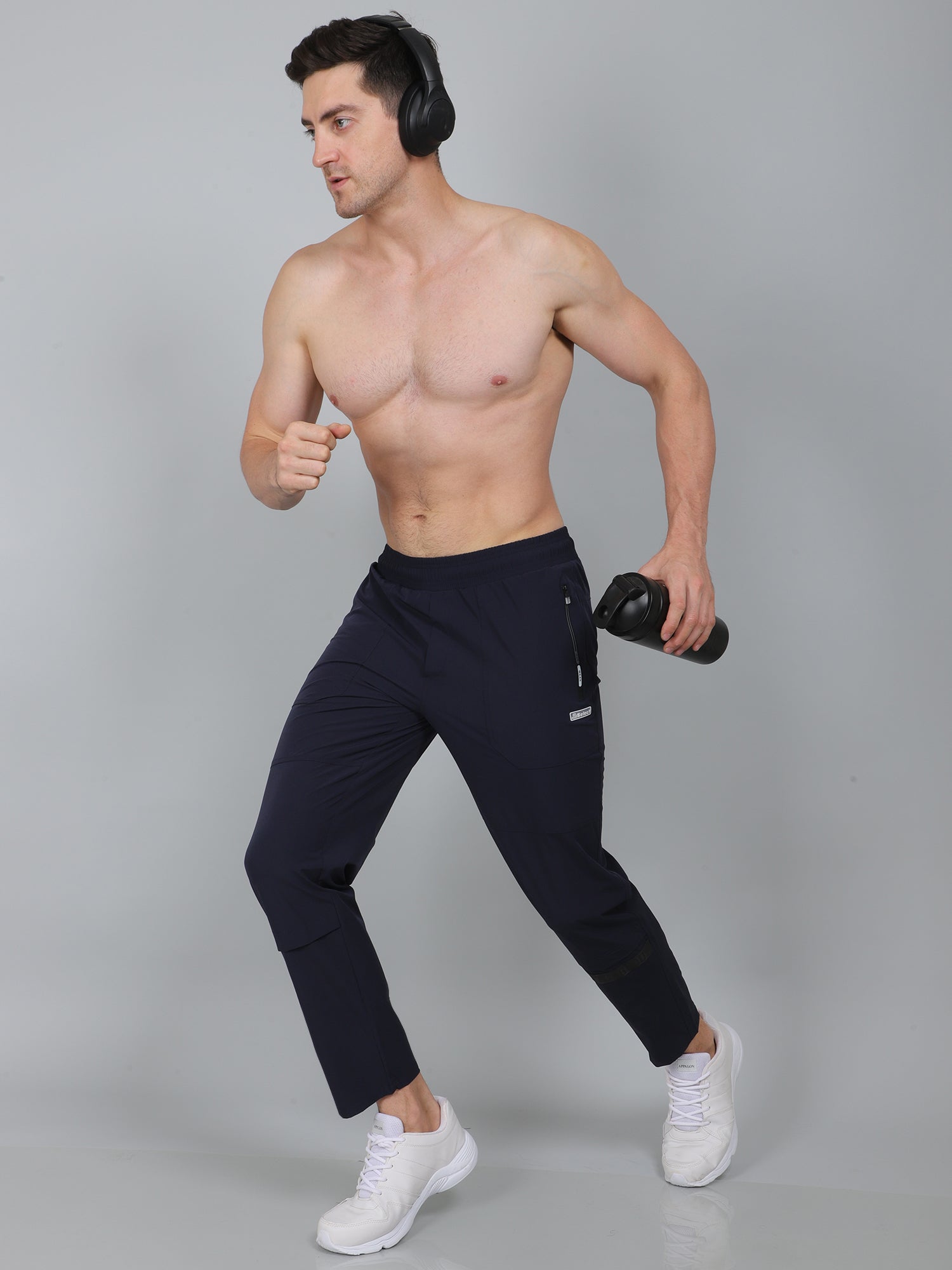 Man in navy jogger pants holding a dumbbell against a gray background