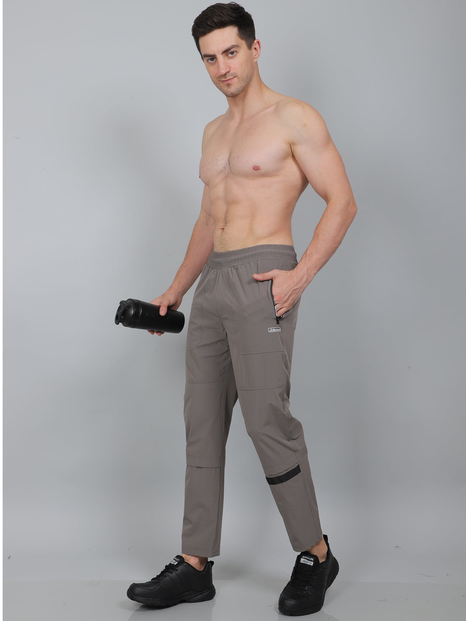Man wearing gray pants holding a camera on a plain background