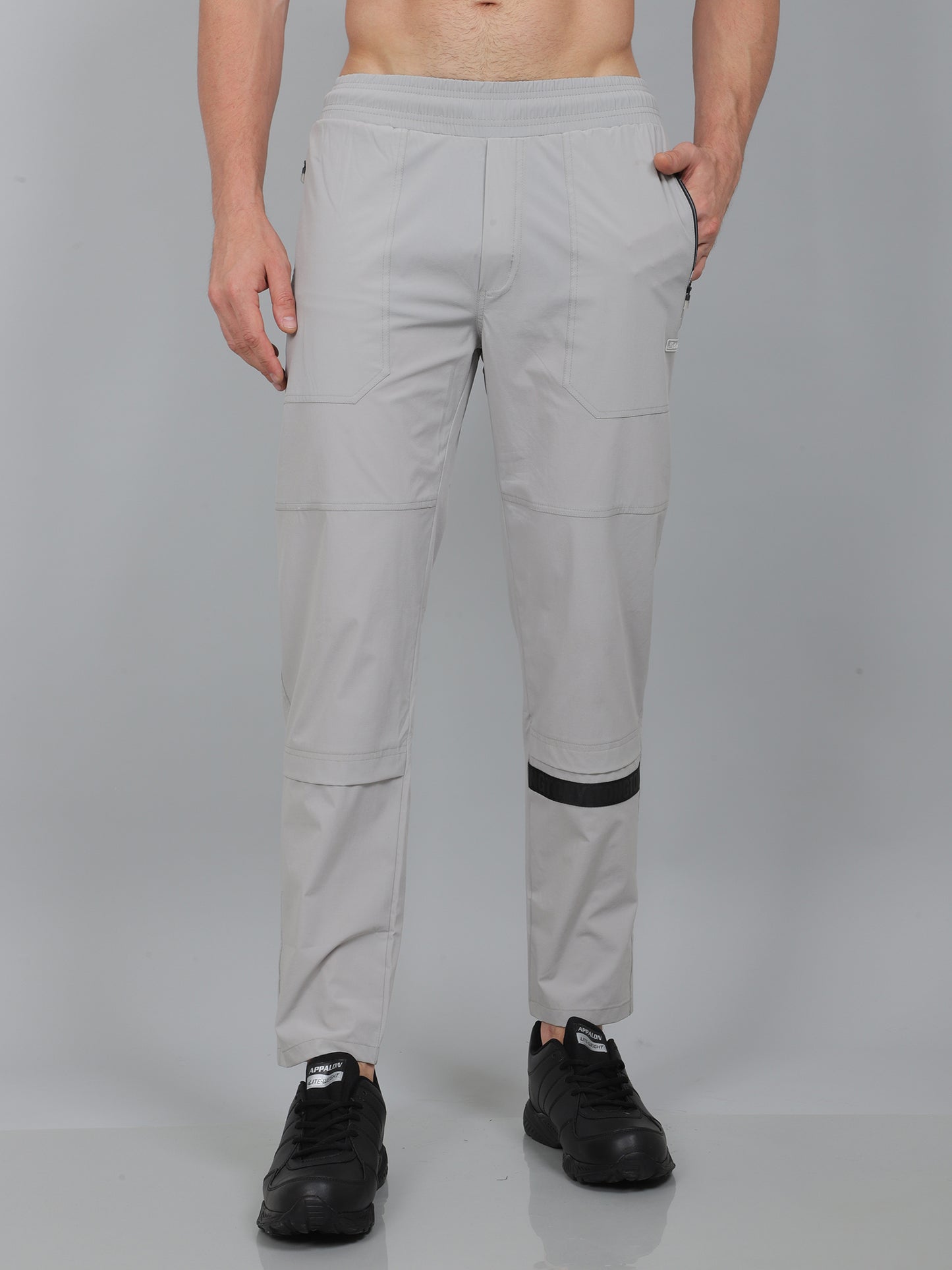 Person wearing light gray pants with black accents on a plain background