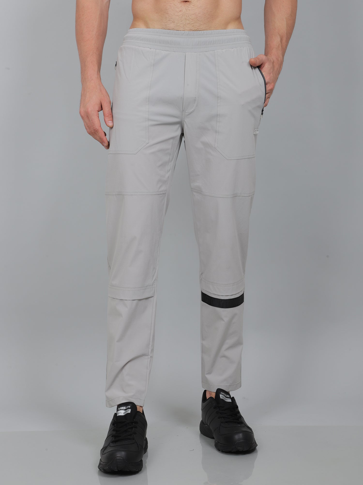 Person wearing light gray pants with black accents on a plain background
