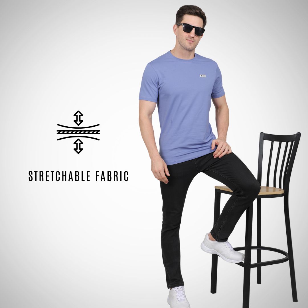 Man wearing a light blue t-shirt and black pants sitting on a bar stool with 'Stretchable Fabric' text and logo.