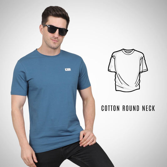 Man wearing a blue t-shirt with a small logo, sunglasses, and black pants on a light gray background.